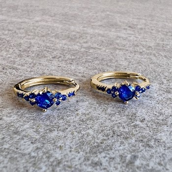 Guld hoop øreringe med en stor blå zirkonia i midten og mindre blå sten langs kanten.